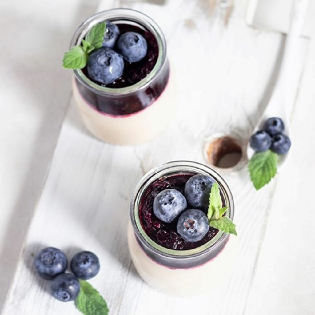 Panna Cotta mit Heidelbeer-Pürree und frischen Heidelbeeren wird in kleinen Dessert-Gläschen serviert