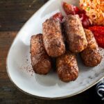 Cevapcici werden auf einer weißen Platte mit Djuvecreis serviert.