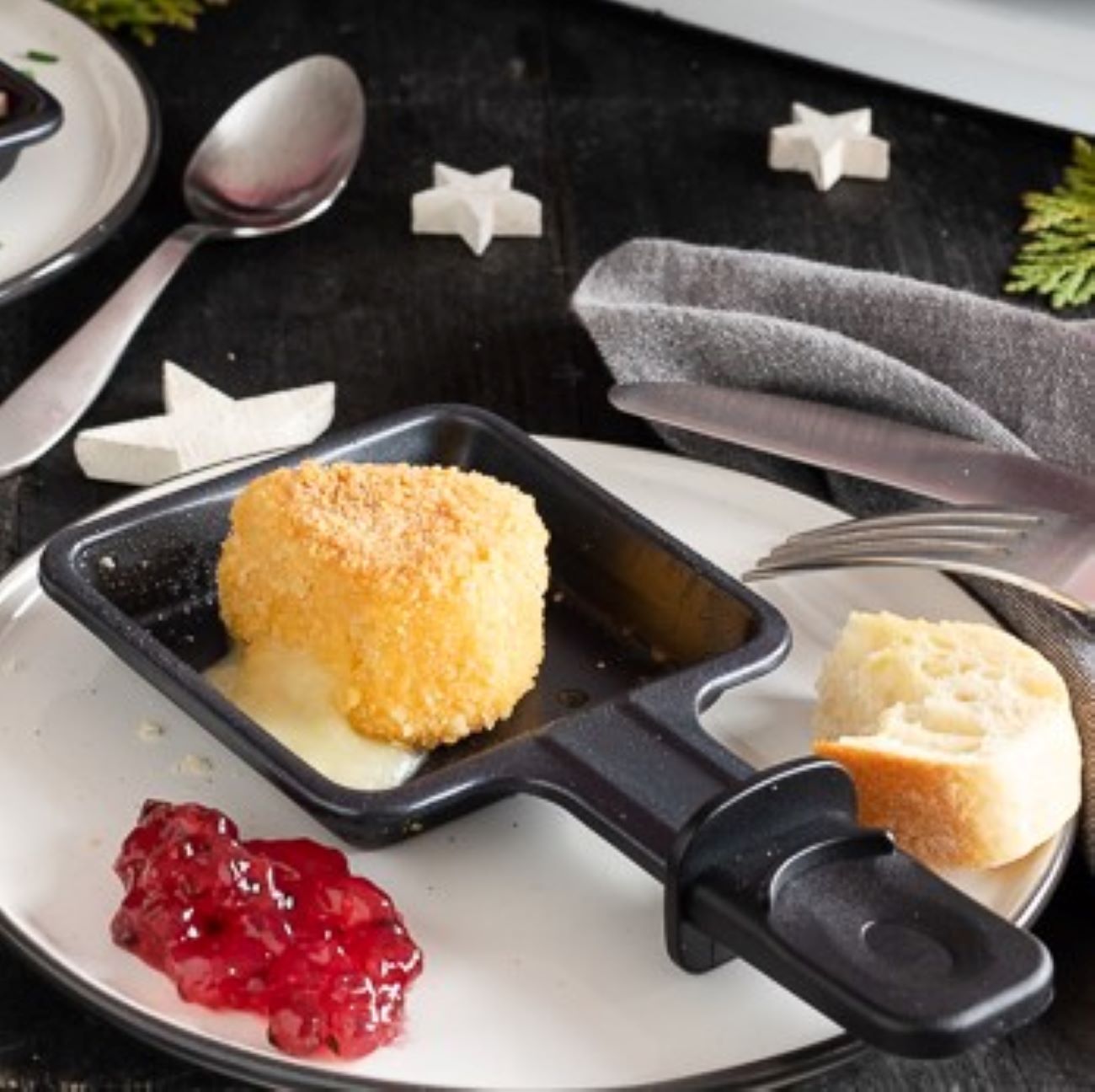 Raclette-Camembert wird auf einem Teller im Pfännchen gezeigt, dazu Preiselbeeren.