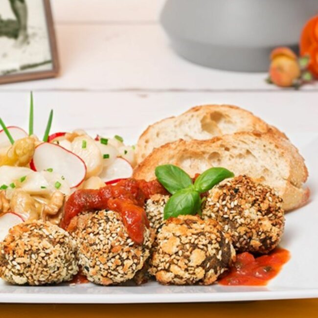 Quinoa-Bällchen werden mit Tomatensauce und Spargelsalat serviert.