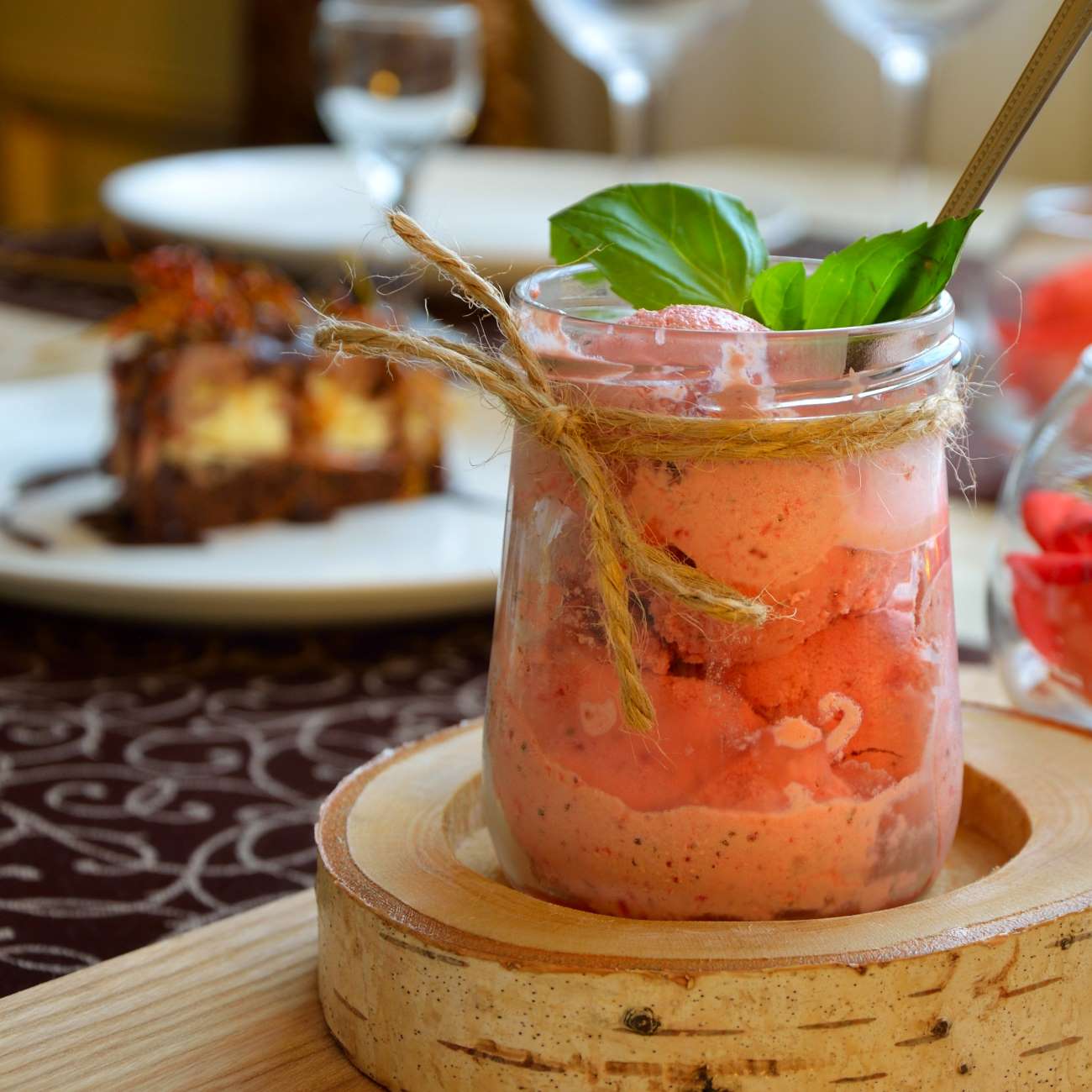 Erdbeer-Sorbet mit Basilikum wird in einem Weckglas auf einer Holzscheibe serviert.