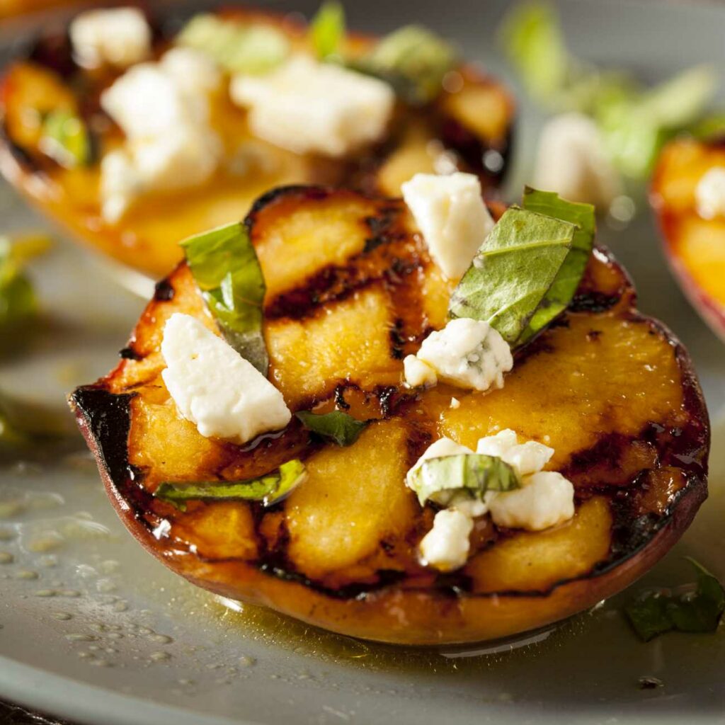 Pfirsiche grillen: Gegrillter Pfirsich wird mit Feta und Basilikum garniert gezeigt.