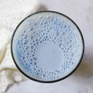 Blaue Mandelmilch wird von oben in einem Glas auf einem grauen Untergrund gezeigt.