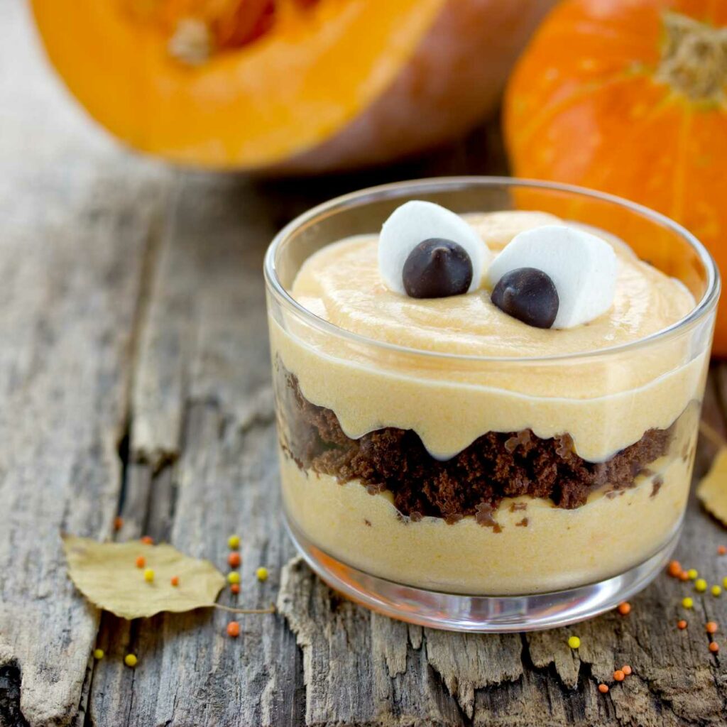 Halloweenský dezert v pohári s marshmallow očami je zobrazený na drevenom pozadí.