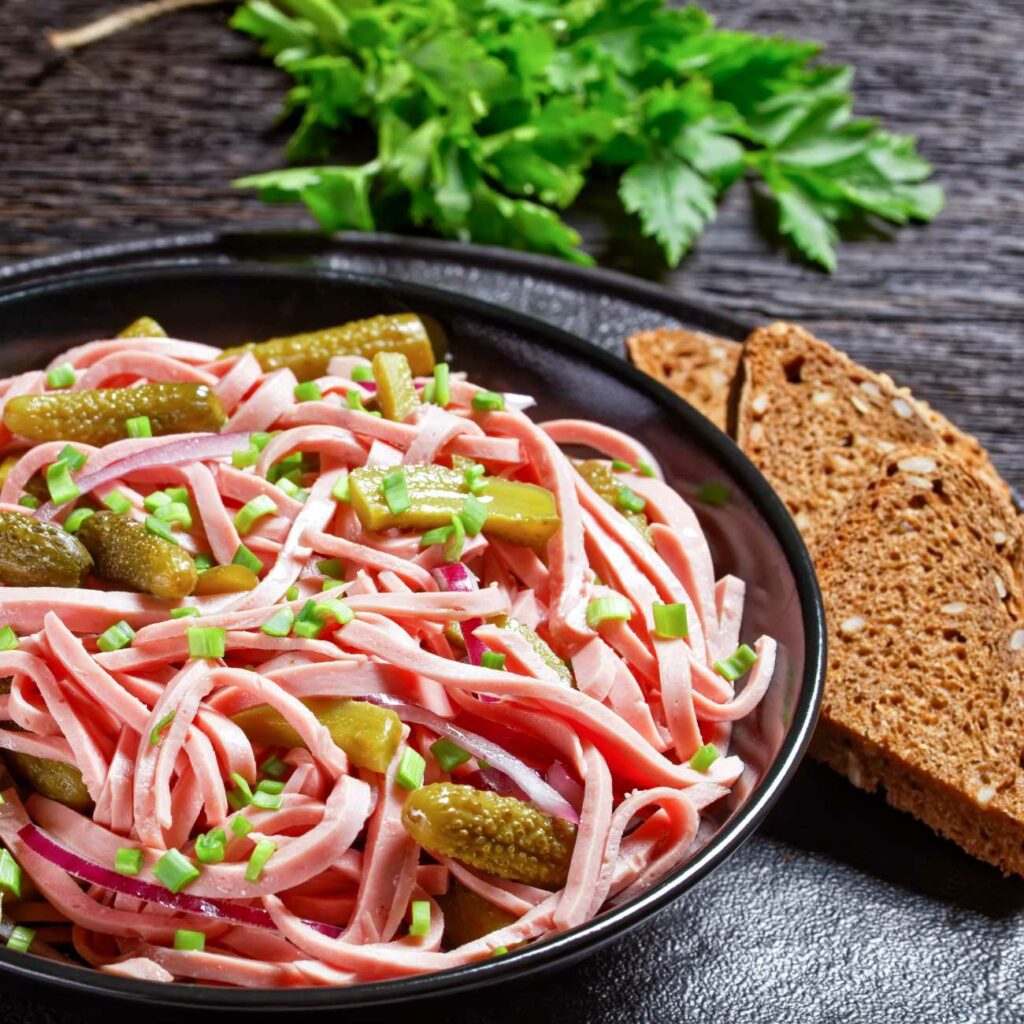 Wurstsalat wird in einer dunklen Schale mit Brot serviert.