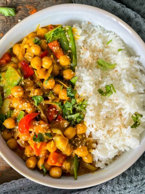 Kichererbsen-Curry wird mit Reis in einer Schale, getoppt mit Sesam und Koriander serviert.