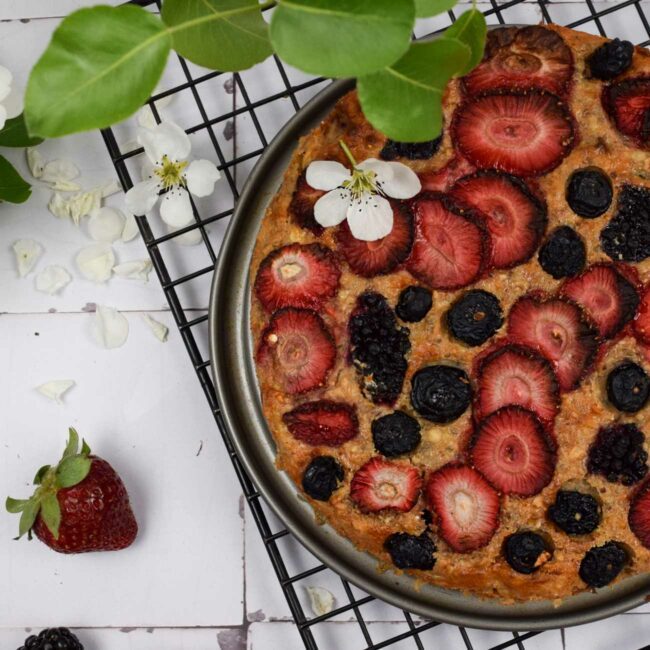 Baked Oats aus der Heißluftfritteuse werden auf einem Kuchengitter mit Blumen und Beeren gezeigt.