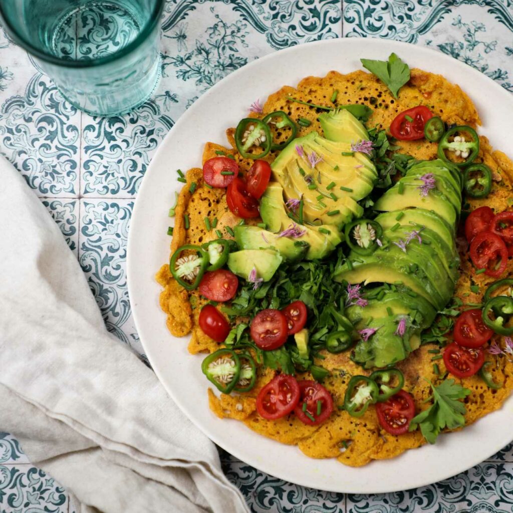 Veganska omleta s solato in avokadom je prikazana na krožniku na pisanih ploščicah.