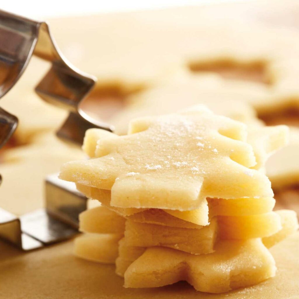 Plätzchenteig wird ausgestochen und gestapelt als Plätzchen bereit zum Backen gezeigt.