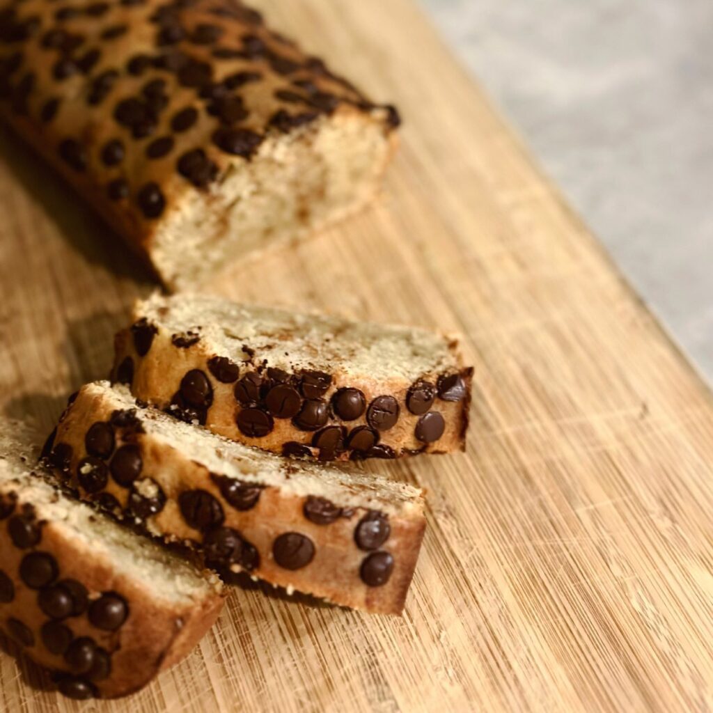 Bananebrot mit Schokotropfen wird auf einem Holzbrett angeschnitten serviert.