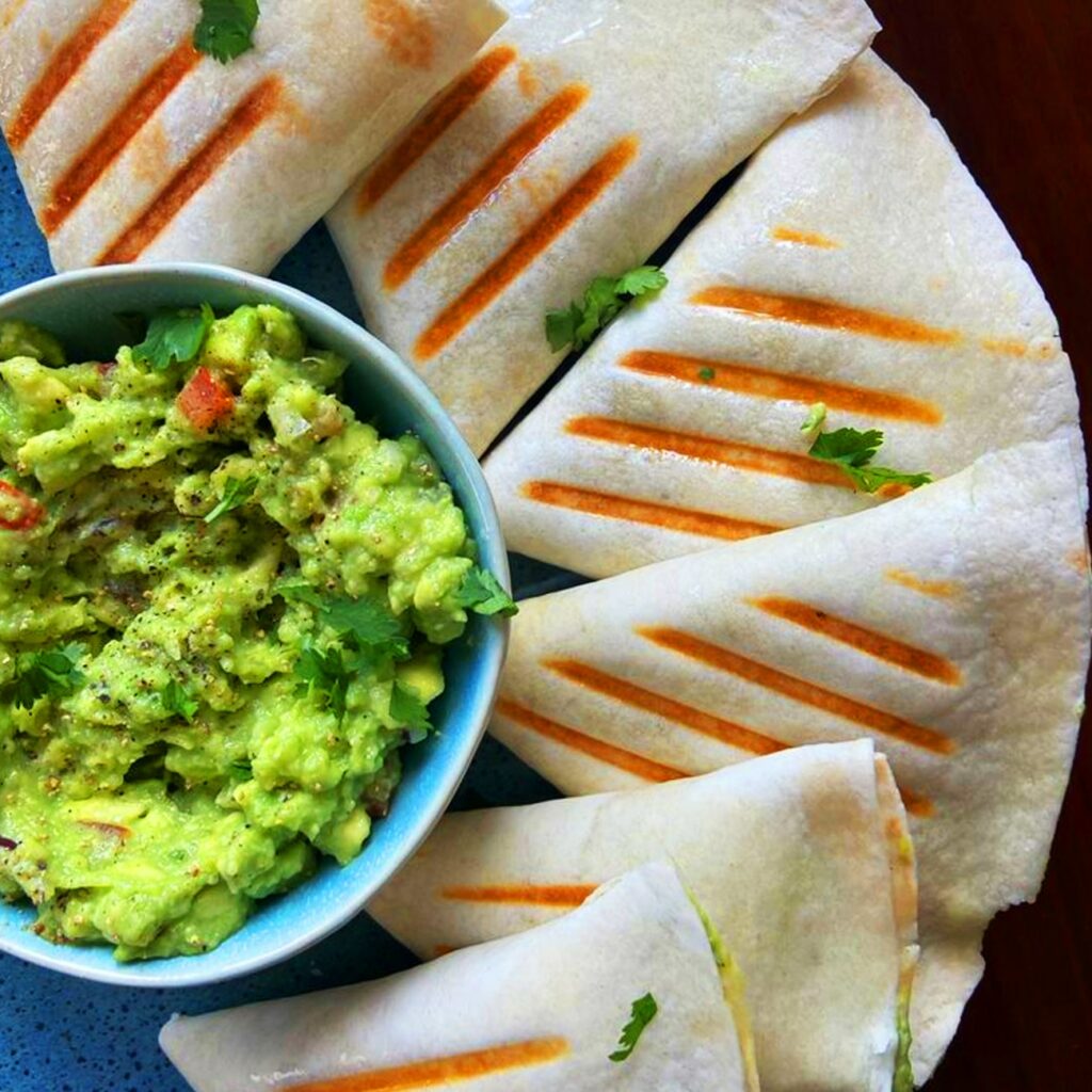 Tortilla Taschen mit Guacamole werden auf einem Teller mit Guacamole gezeigt.