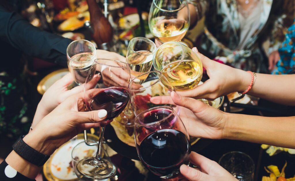 Ludzie trzymają różne kieliszki do wina i wznoszą toasty nad zastawionym stołem