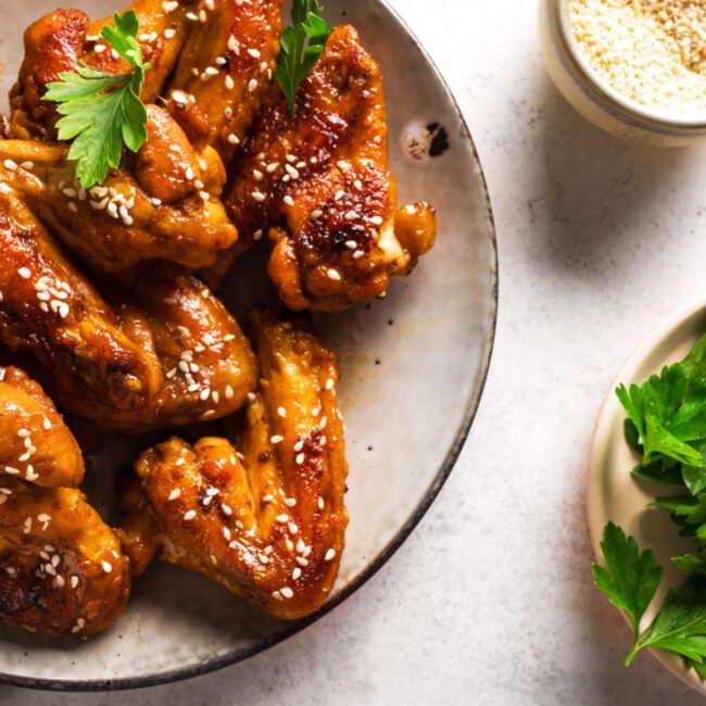 Chicken Wings aus der Heißluftfritteuse werden mit Koriander und Sesamsamen auf einem weißen Teller serviert.