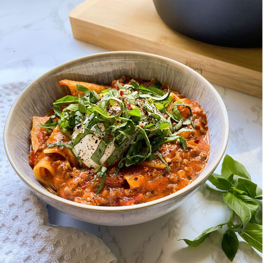 Lasagnesuppe wird in einem tiefen Teller mit Mozzarella, Basilikum und Ricotta garniert serviert.