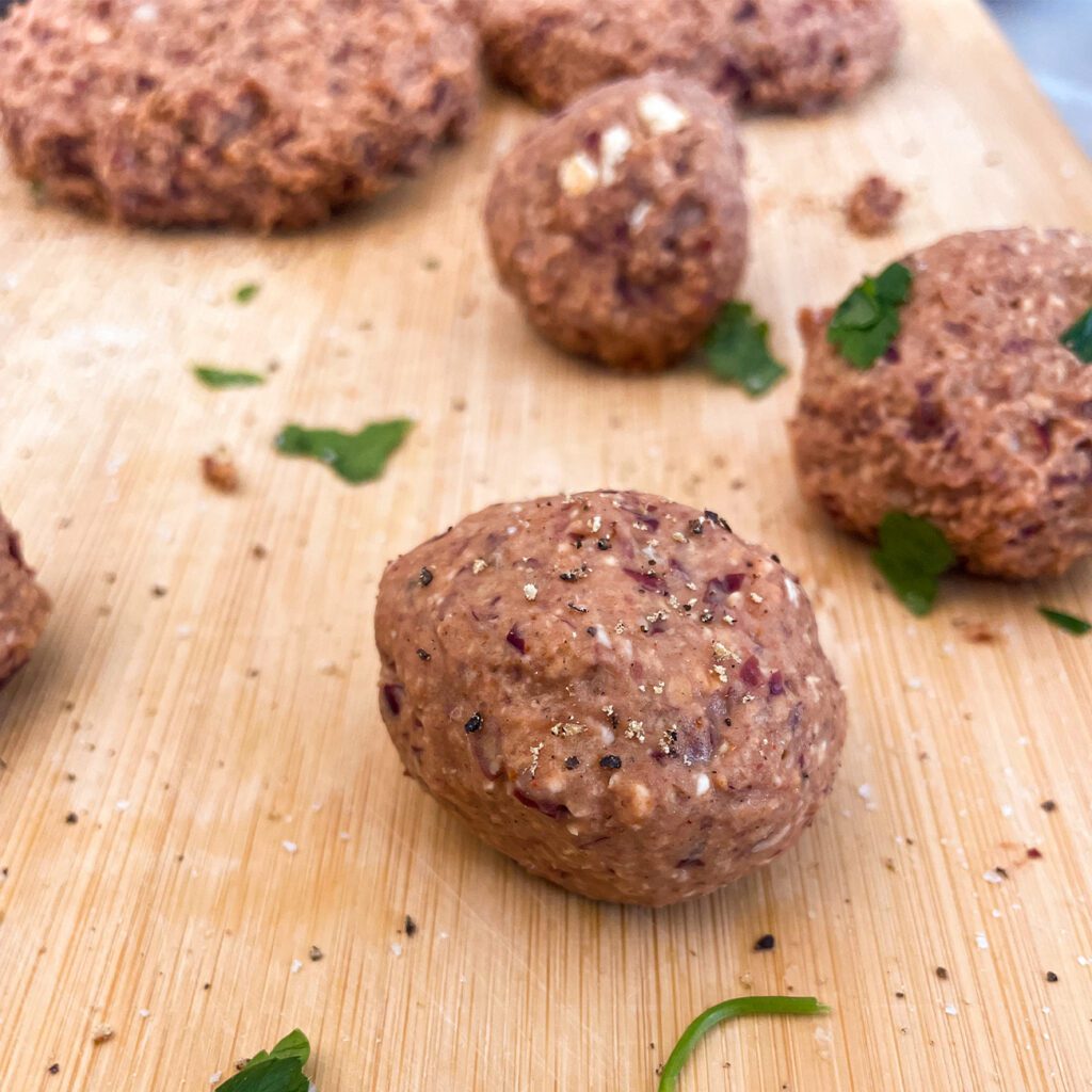 Veganes Hackfleisch wird in verschiedenen Zubereitungsformen auf einem Holzbrett gezeigt.