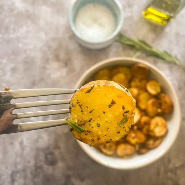 Rosmarinkartoffeln werden in einer Schale auf dunklem Untergrund gezeigt.