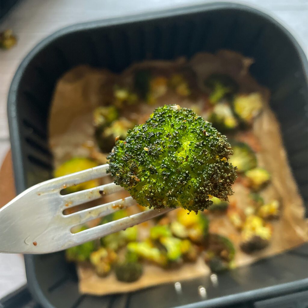 Brokolica z fritézy sa drží na vidličke v blízkosti kamery. Panvica fritézy je pod ňou rozostrená.